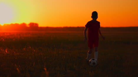 Junge-Fußballspieler-Läuft-Bei-Sonnenuntergang-Mit-Einem-Fußball-Auf-Dem-Feld-Und-Trainiert-Von-Morgens-Bis-Abends-Dribbelt.-Weg-Zum-Erfolg.-Das-Konzept,-Das-Ziel-Eines-Erfolgreichen-Sportlers-Zu-Erreichen